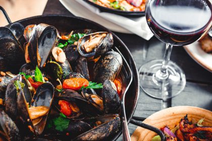 A bowl of mussels on a table with a glass of red wine. A blog image for dining out