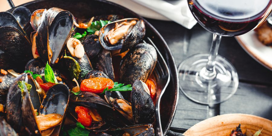 A bowl of mussels on a table with a glass of red wine. A blog image for dining out