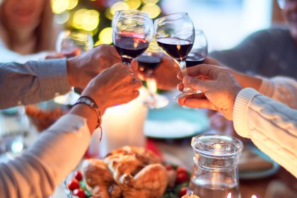 People hosting guests for dinner. Holding up glasses of red wine over a feast.