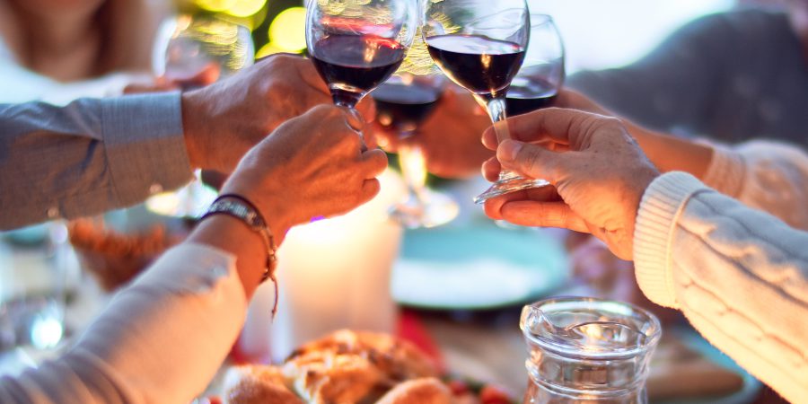 People hosting guests for dinner. Holding up glasses of red wine over a feast.