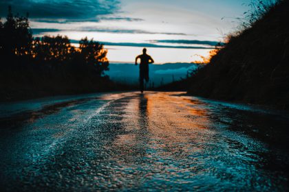 A man running on a road to the first rays of an early sunrise, symbolizing commitment to a exercise routine