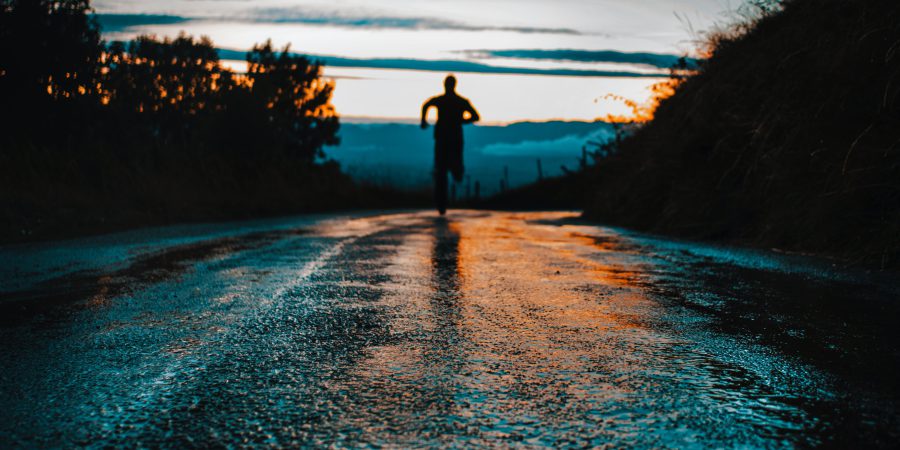 A man running on a road to the first rays of an early sunrise, symbolizing commitment to a exercise routine