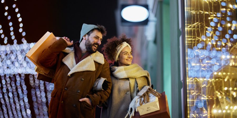 Young happy couple enjoying in a night walk through the city while buying Christmas presents - Our top consumer tips for the holidays
