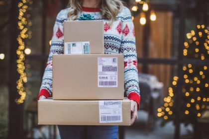 Person holding packages in front of a porch with holiday decor - Holiday shopping online? Here’s how to protect yourself